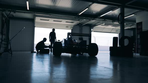 Servicemen are Repairing a Racing Car in a Garage alt