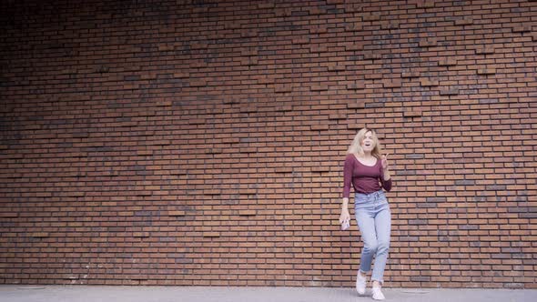 Pretty Woman Counts and Dances Near Red Brick Wall on Street