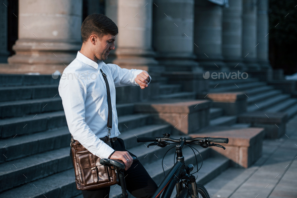 Time to go. Businessman in formal clothes with black bicycle is in the city