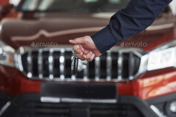 Hand with keys. Man in official clothes stands near his new car in automobile salon