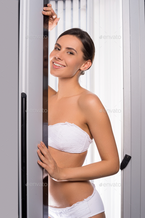 Beautiful woman in solarium. Attractive young woman looking out of tanning booth and smiling