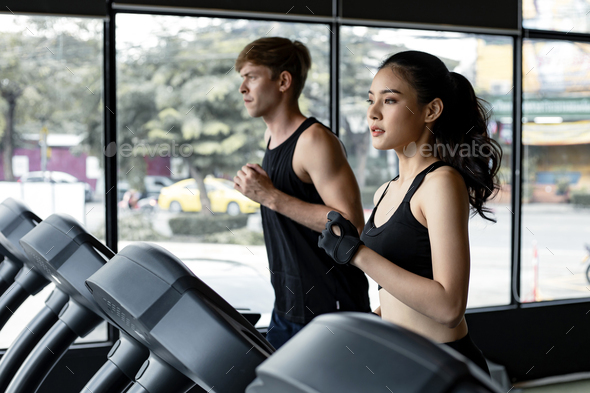 Young woman and man running side by side on modern electric treadmills.
