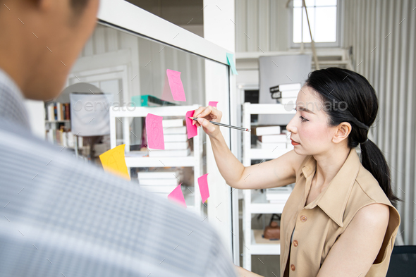 Business woman with use post it notes on clear board to share idea working.