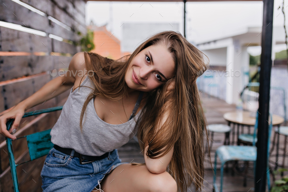 Dark-eyed woman in denim skirt playing with her hair in outdoor cafe. Pretty  brunette female model Stock Photo by look_studio