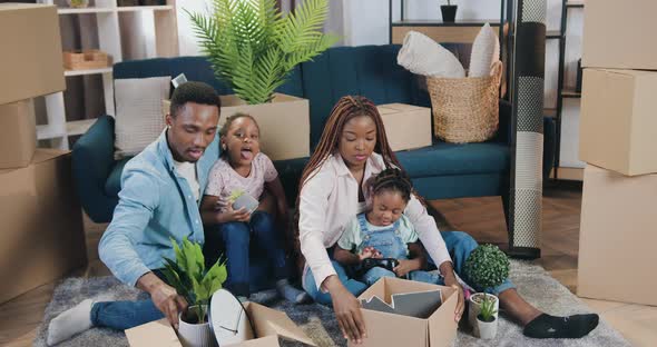 African American Couple with Kids Sitting on the Floor and Unpacking Boxes in Newly Acquired alt