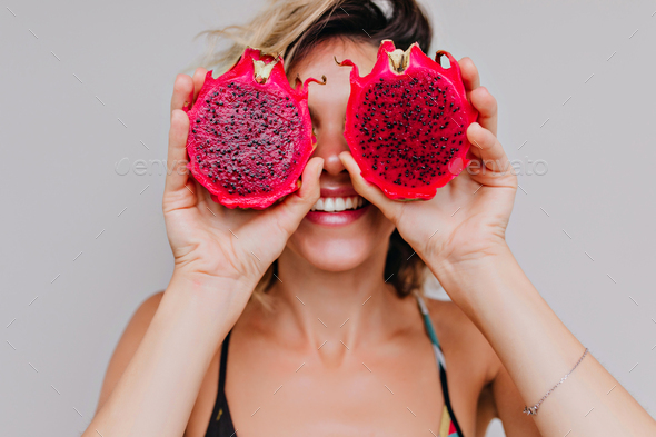 Close-up portrait of good-looking young woman fooling around during photoshoot with dragon fruits.