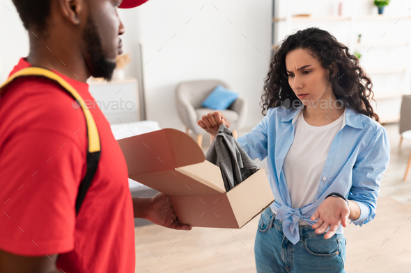 Confused frustrated lady unpacking box, holding clothes