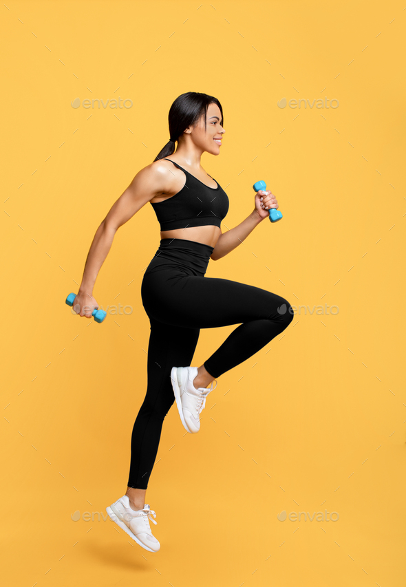 Workout concept. Full length shot of young black woman in sportswear exercising with two dumbbells