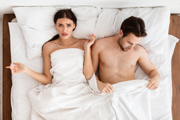 Displeased Girlfriend Lying Near Boyfriend With Erectile Dysfunction In Bedroom