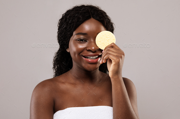 Skin Care Concept. Attractive Black Lady Covering Eyes With Cosmetic Sponge
