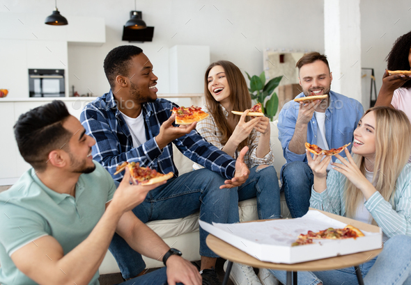 laughing friends eating pizza and having fun. They are enjoying eating and  drinking together Stock Photo
