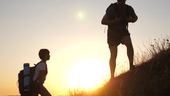 Travelers with Children Travel at Sunset. Father Holds Out His Hand Helping Children Climb Mountain alt