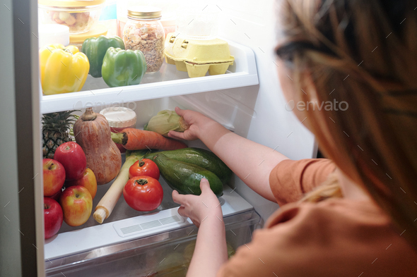 Woman reaching for vegetables in refrigerator
