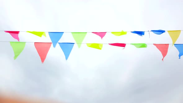 Multicolored triangular flags hang on a string and flutter in the wind against a cloudy cloudy sky.