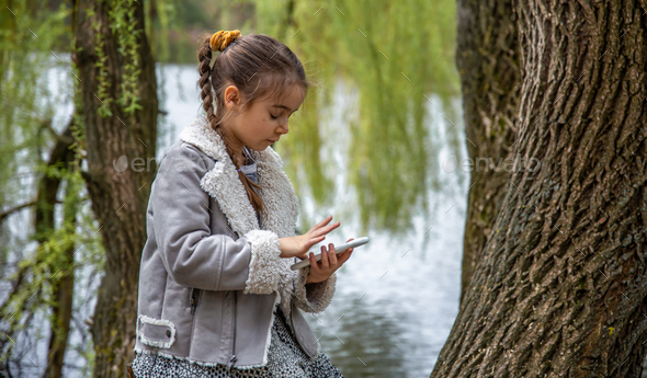 A little girl on a walk checks her phone, not paying attention to anything.