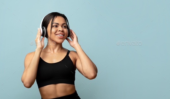 Active free time. Sporty black lady in sports uniform with headphones exercising or dancing, blue