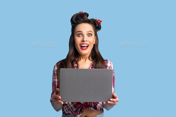 Young pinup lady in retro clothes holding laptop, feeling excited over huge sale in webstore