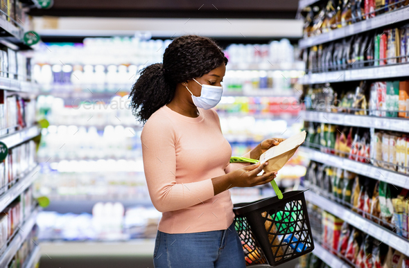 Lovely African American woman in face mask making choice of products at supermarket during