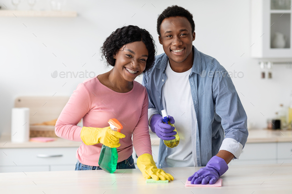 Positive black couple cleaning up together, vacuuming under carpet