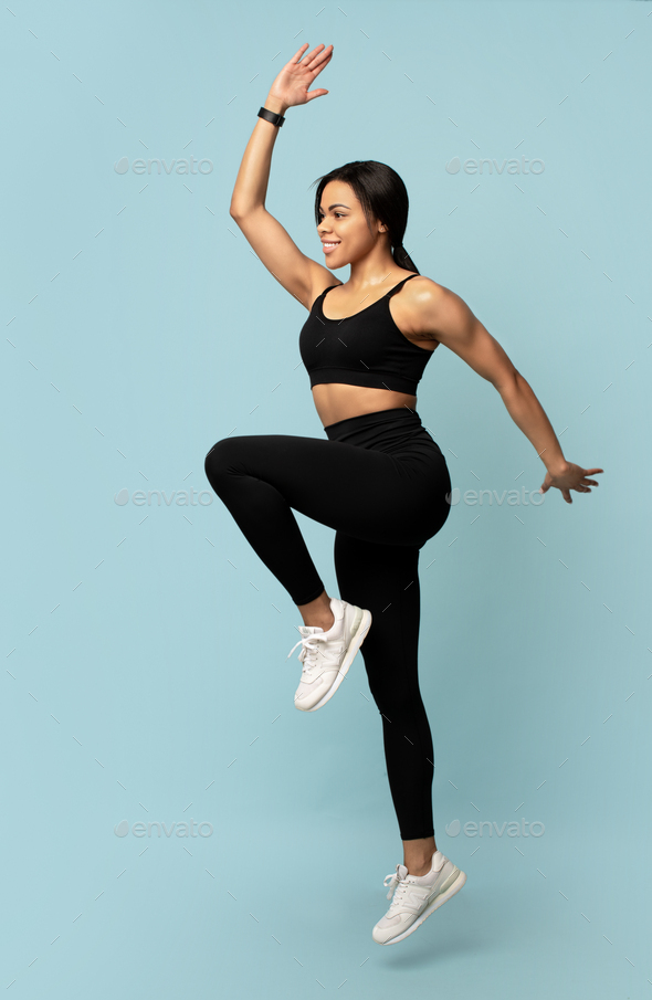 Sport concept. Young african american lady jumping, exercising and lifting leg up over blue