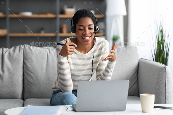 Online Tutoring. Cheerful African Lady In Headset Making Virtual Meeting On Laptop