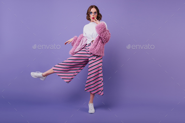 Surprised lovely girl in white shoes posing on purple background during indoor  photoshoot. Full-len Stock Photo by look_studio