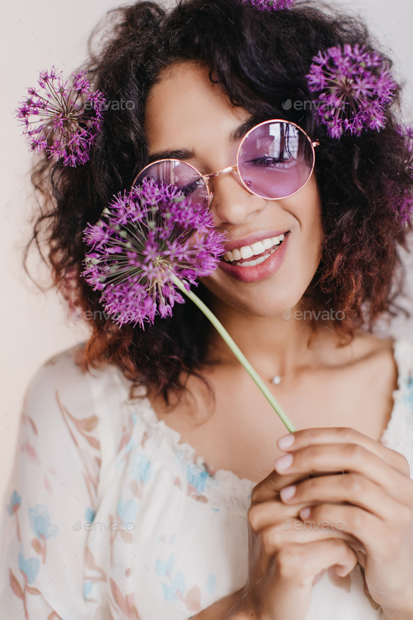 Close-up portrait of relaxed african girl posing with purle flower. Indoor shot of pretty black wom - Stock Photo - Images