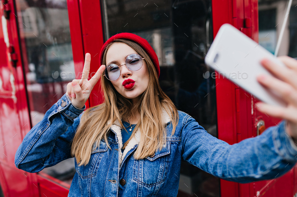 Lovely young woman with red lips making selfie in spring day and using phone. Outdoor portrait of e - Stock Photo - Images