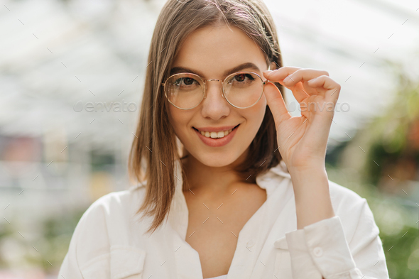 Portrait of pretty smiling teen girl wearing round glasses looking at  camera outdoors on blurred landscape background with copy space in spring  day. Stock Photo