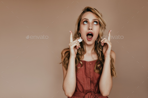 Surprised long-haired woman looking up with mouth open. Lovely blonde female model expressing amaze