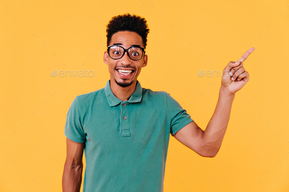 Handsome african boy in big glasses expressing amazement. Indoor shot of emotional male model with