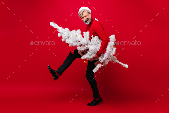 Excited grandpa having fun in studio. Carefree old man funny dancing and holding christmas tree