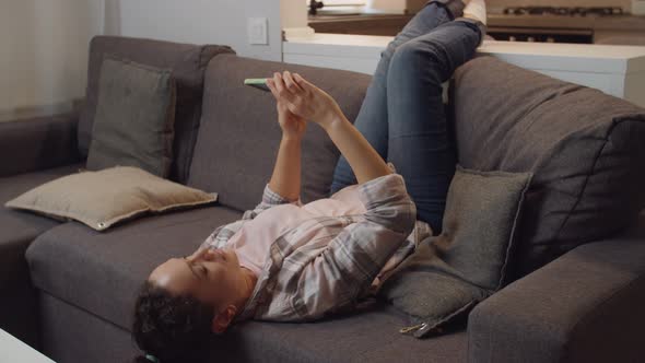 Adult Woman Taking Selfie Using Mobile App While Lying on Couch Indoor alt