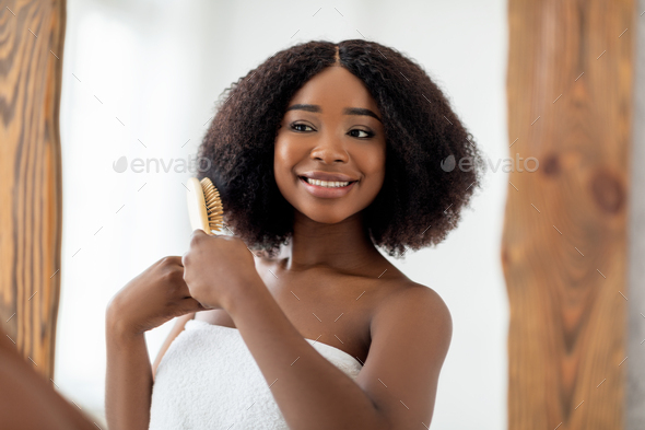 Smiling African American woman brushing her hair in front of mirror at home