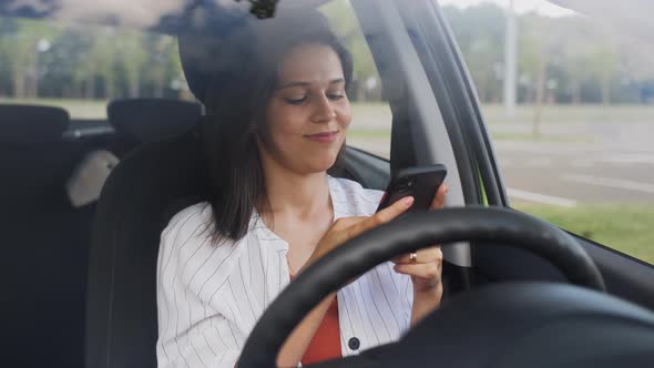 A Girl with a Smartphone in Her Hands is Driving a Car