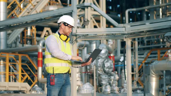 Engineer with a Laptop is Managing the Refinery Working Process alt