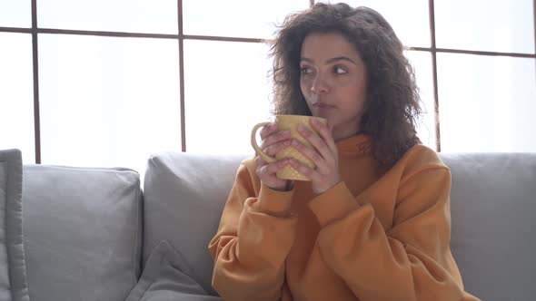 Happy Young Hispanic Woman Relaxing on Comfortable Sofa Drinking Tea at Home alt