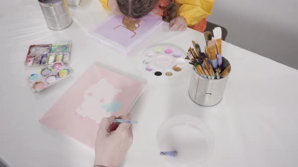 Little girl painting with acrylic paint on canvas with her mother for a distant learning art project alt