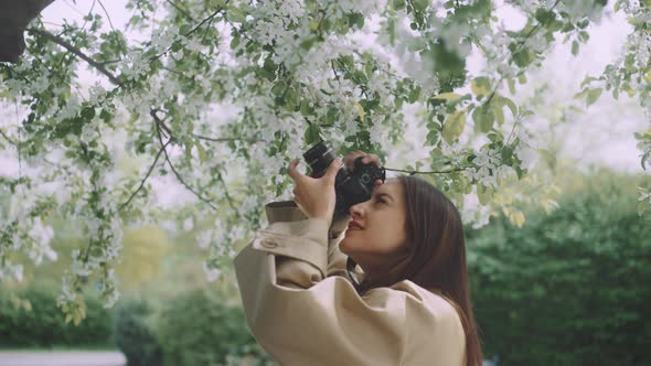 Young woman taking pictures with camera standing under a blossoming tree alt