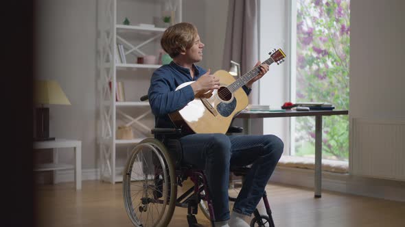 Happy Talented Songwriter Playing Guitar Singing Sitting in Wheelchair at Home in Living Room alt