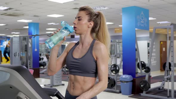 Young sporty Woman On Running Machine In Gym drinking water alt