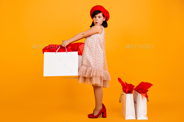 Adorbale preteen girl in mom\'s shoes posing with shopping bags. Studio shot of caucasian kid in dre