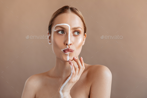 Gray-eyed girl with white stripe on her face and arm bit her lip in anticipation and posing on beig