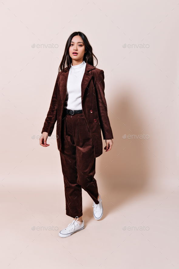 Asian woman in corduroy suit looks into camera on beige background