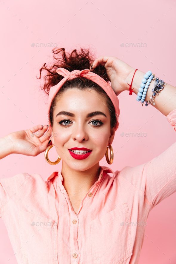 Close-up portrait of blue-eyed lady with red lipstick dressed in pink shirt and massive earrings on