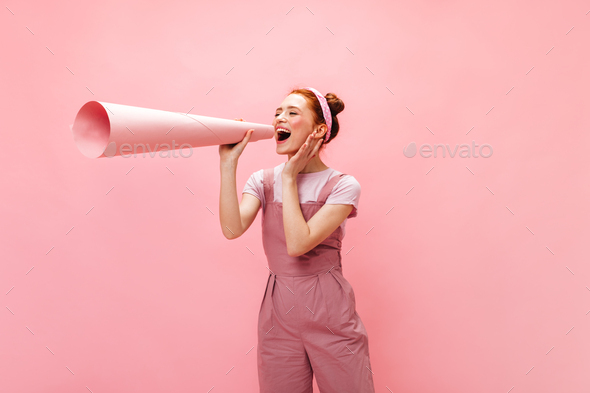 Woman in pink outfit attached to her ear huge piece of paper rolled into tube