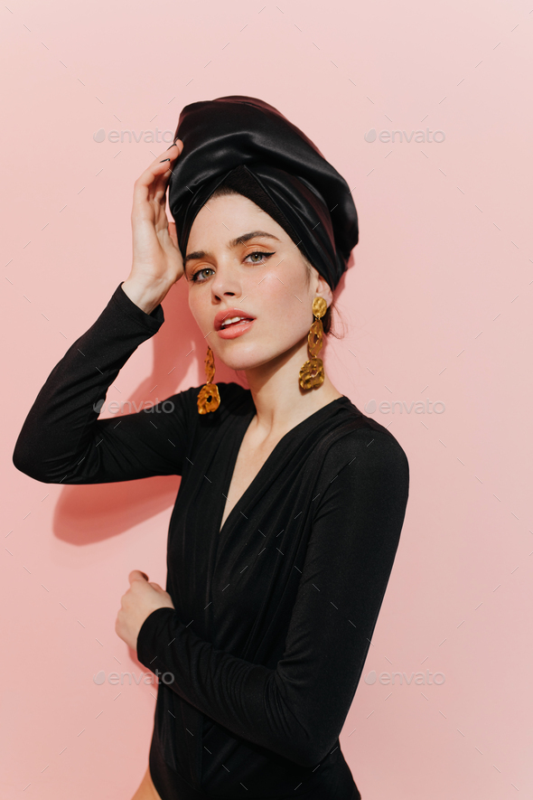 Interested young lady touching turban. Studio shot of fashionable girl wearing golden jewelry.