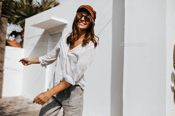 Pretty girl in summer blouse and linen pants walks outside. Portrait of woman in sunglasses and bro