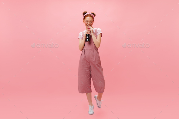 Charming lady in pink jumpsuit and white t-shirt throws up like sign. Girl in pink glasses posing o