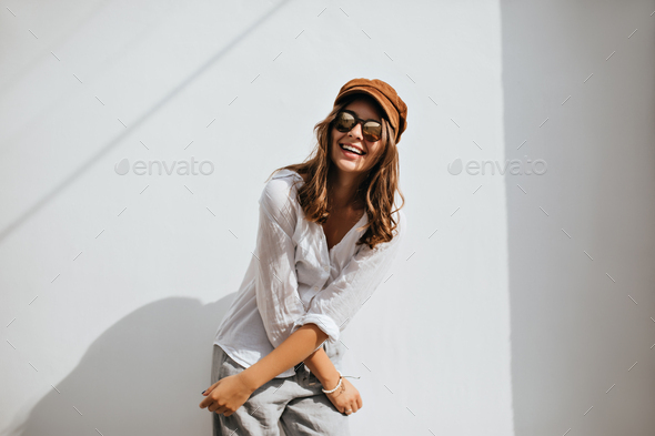 Fashionable girl in glasses with mirrored lenses and corduroy cap is smiling. Woman in light clothe